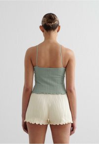Top scurt ribbed de culoare verde deschis cu bretele subțiri, asortați cu pantaloni scurți texturat de culoare alb-off cu margini ondulate.
