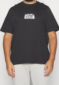 Svart bomullströja med en rektangulär grafisk logotyp i vitt och grått. Kortsleeves, rund halsringning, avslappnad passform och slät textur.