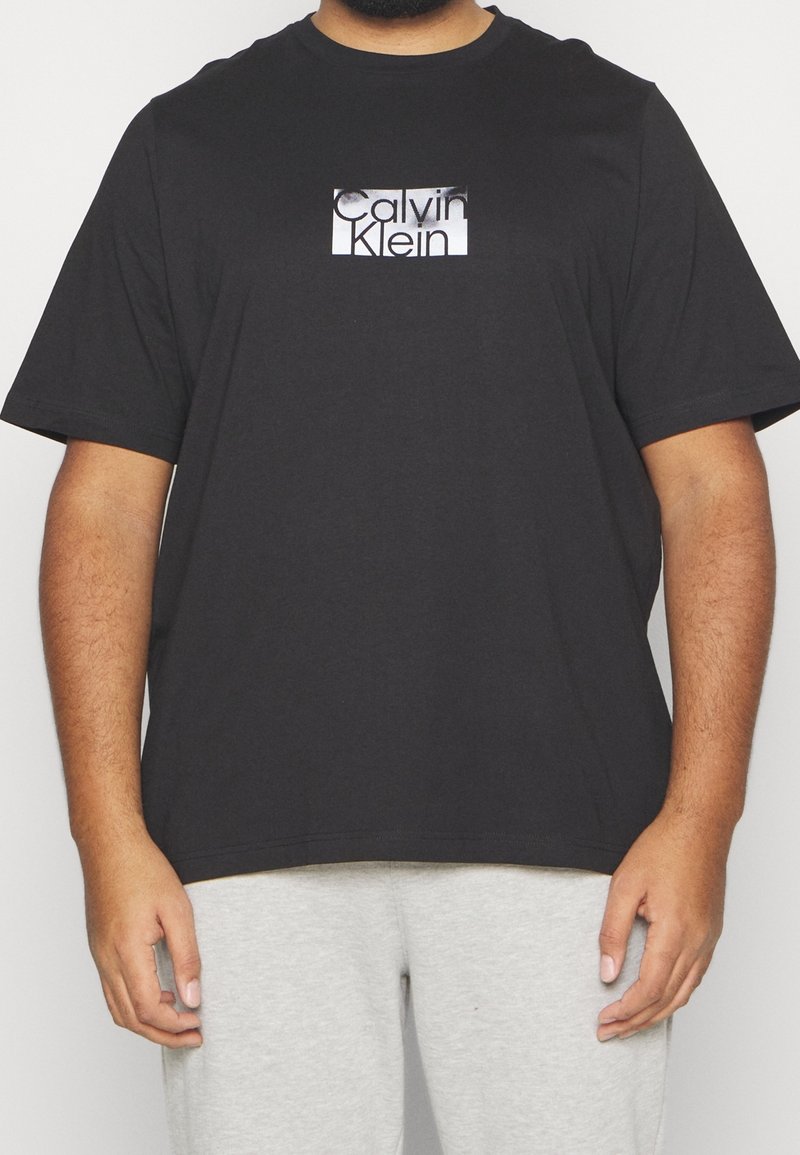 Svart bomullströja med en rektangulär grafisk logotyp i vitt och grått. Kortsleeves, rund halsringning, avslappnad passform och slät textur.