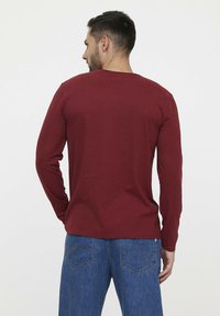 Een rood shirt met lange mouwen en een ronde halslijn, gemaakt van zachte stof. Gecombineerd met lichtblauwe jeans met een ontwerp van een achterzak.