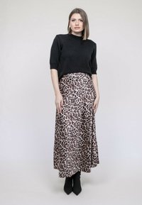 Pull en tricot noir à manches courtes associé à une longue jupe en satin imprimé léopard et des bottines noires à talons pointus.