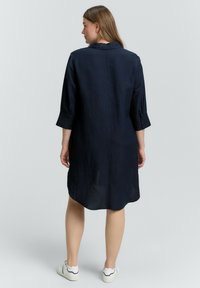 Abito camicia blu navy, lunghezza al ginocchio, in tessuto leggero con maniche a tre quarti, polsini con bottoni e orlo leggermente curvo.
