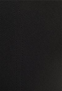 Gros plan sur un tissu tricoté noir avec une texture côtelée et une couture diagonale formant un motif chevron subtil.