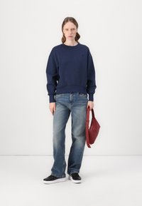 Mörkblå sweatshirt med avslappnad passform, ribbade ärmslut och midja. Matchad med ljusblå jeans och svarta sneakers. Accessoarer i form av en röd väska.