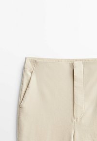 Pantalon en velours côtelé beige avec poche latérale et braguette avant zippée couverte sur fond blanc.