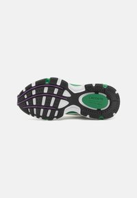 Lacoste athletic shoe sole featuring black rubber, green and purple accents, textured patterns, and a white midsole with drainage holes.
