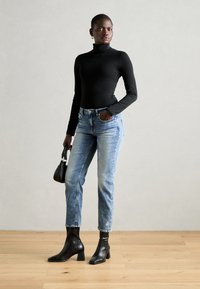 Schwarz langärmeliges eng anliegendes Oberteil, hellblaue hochgeschnittene Jeans und schwarze Ankle Boots mit Blockabsatz. Kleine florale Details auf den Jeans.