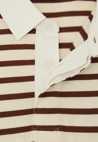 Beżowa koszulka polo z brązowymi paskami, złożonym kołnierzykiem i dwoma guzikami przy dekolcie. Struktura tkaniny jest gładka i dzianinowa.