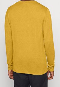 Långärmad tröja med rundad hals i senapsgul, tillverkad av mjuk bomullsblandning. Har en något avslappnad passform och ribbade muddar.