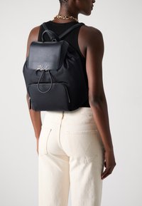 Mochila de nylon negra con un diseño estructurado, bolsillo frontal con cremallera y el logo "Karl" característico en plata. Correas ajustables y textura suave.