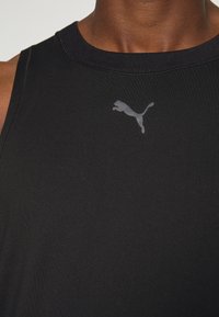 Débardeur de sport sans manches noir en tissu lisse, avec un logo Puma gris brillant subtil sur la poitrine.