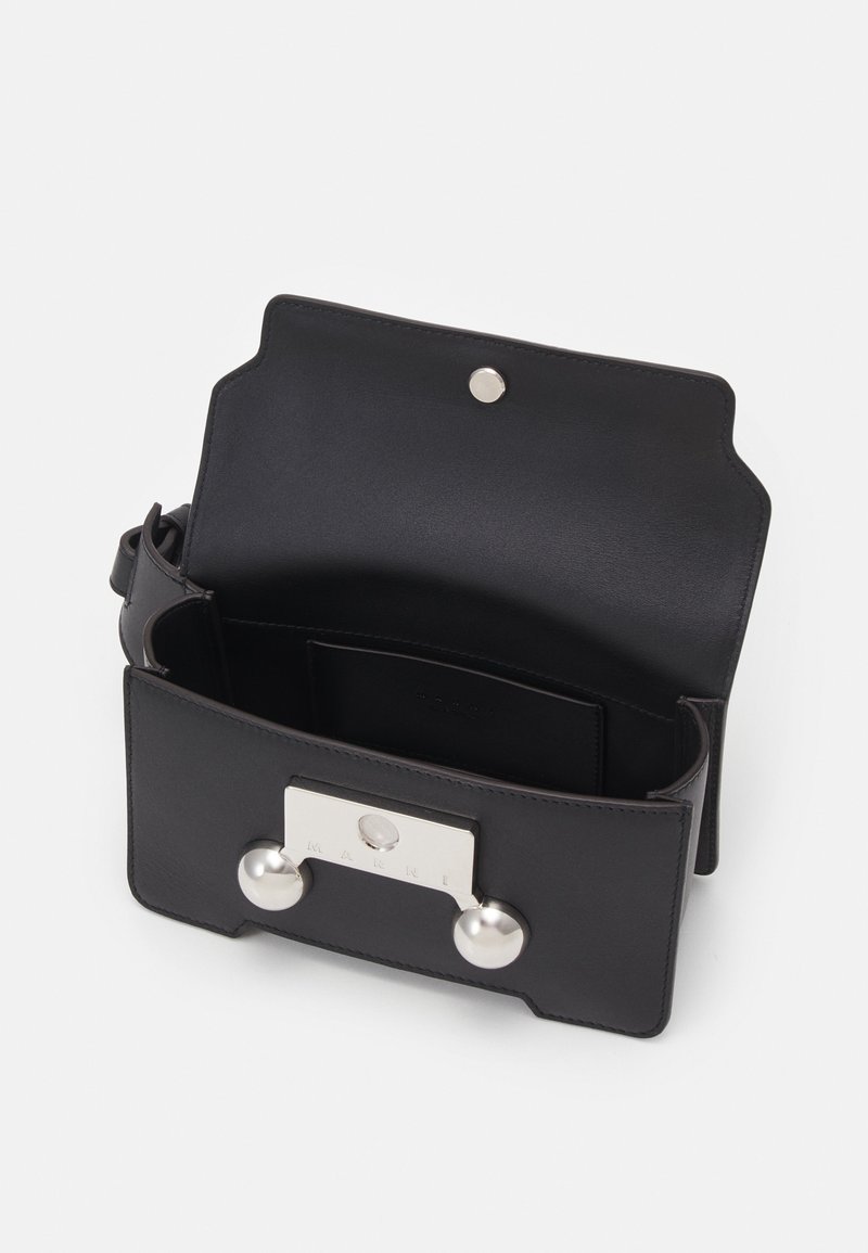 Sac à main en cuir noir avec un design structuré, des accessoires en métal comportant deux accents ronds et une fermeture à pression. L'intérieur comprend un espace pour cartes.