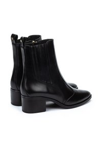 Botas de cuero negro hasta el tobillo con punta afilada, pequeño tacón y acentos acanalados verticales en los laterales. Diseño elegante con detalles minimalistas.