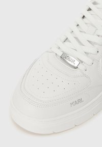 Λευκά αθλητικά παπούτσια από λείες δερματίνες, με τρυπητό δάκτυλο, υφασμάτινες λεπτομέρειες και ασημένιο λογότυπο "KARL" στη γλώσσα. Λευκές επίπεδες γλώσσες.