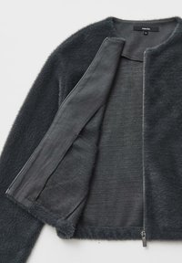 Giacca in pelliccia sintetica di colore grigio scuro con una texture morbida, apertura frontale e chiusura con zip, caratterizzata da un design semplice e privo di motivi distintivi.
