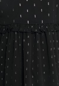 Schwarzes Kleid aus strukturiertem Stoff mit verstreuten metallischen Akzenten. Der Saum hat ein Rüschendetail, das das Gesamtdesign verbessert.