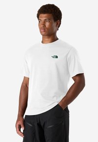 Camiseta blanca de manga corta hecha de algodón, con un pequeño logo verde en el área del pecho izquierdo. Corte recto, textura suave, cuello redondo.