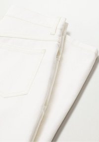 Jean en denim blanc plié montrant la poche arrière, la boucle de ceinture et les coutures visibles sur une surface blanche plane.