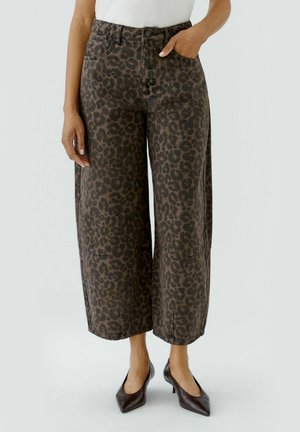 Vrouw draagt cropped wijde broek met donkerbruine luipaardprint, gecombineerd met zwarte puntige hakken en een witte mouwloze top.