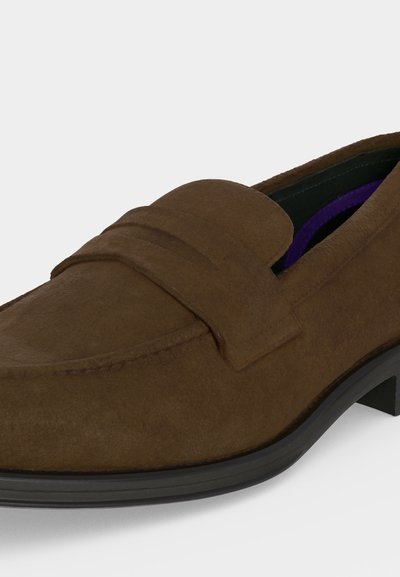 Mocassin homme en daim marron avec semelle noire et petit talon, comportant une bride sur le dessus.