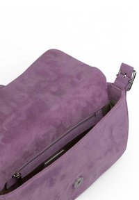 Bolso de ante morado con un diseño relajado. Presenta un bolsillo con cremallera en el interior, textura suave y detalles de hardware plateado.