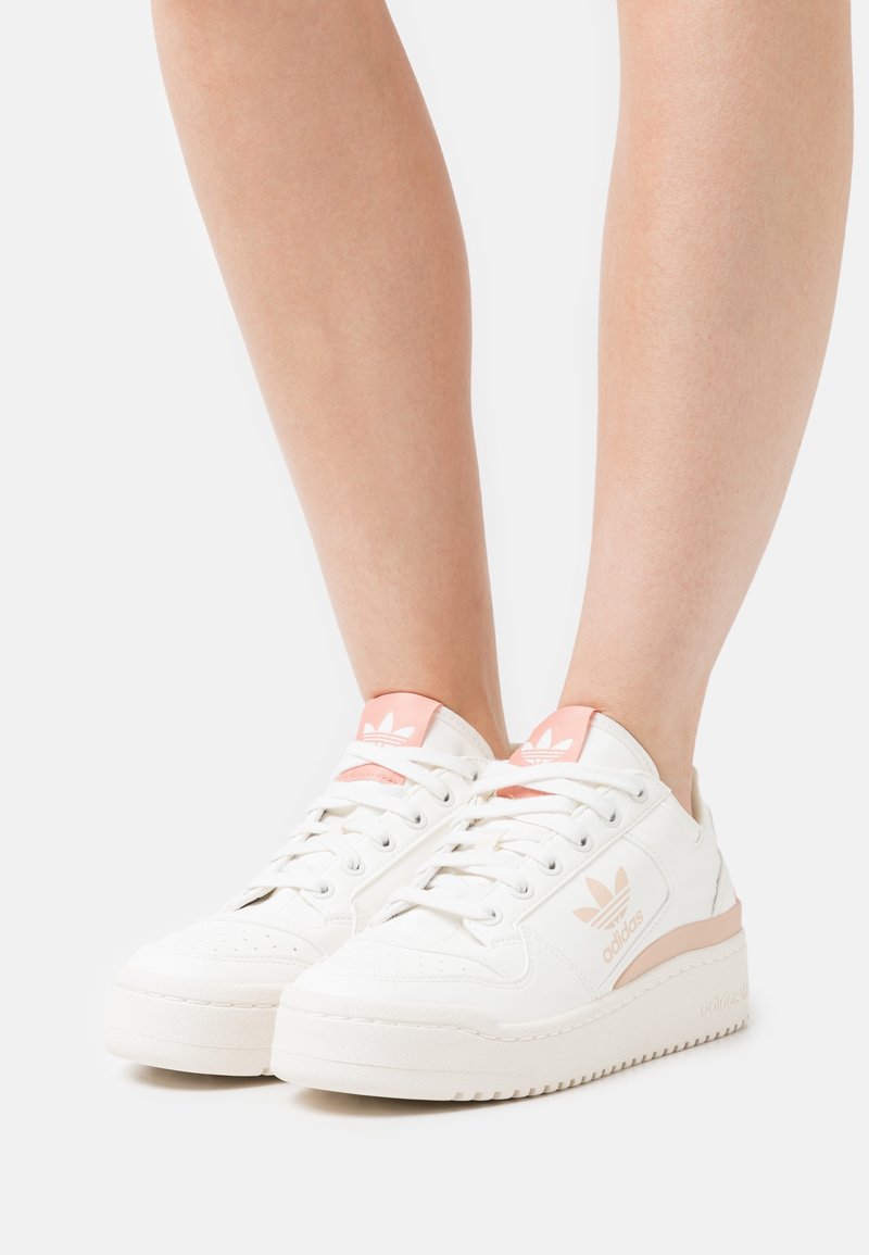 Zapatillas de cuero blanco con detalles en rosa, puntera redonda, diseño con cordones y suela texturizada. Presentan un logo en relieve en el lateral y el talón.