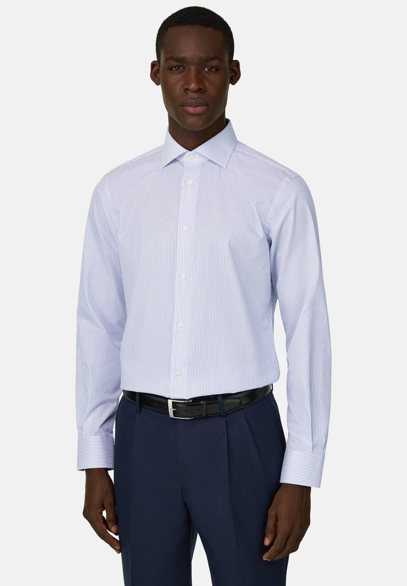 Man draagt een lichtblauw gestreept slim-fit overhemd met witte knopen, gecombineerd met donkerblauwe broek en een zwarte riem, staand in een rechte houding.