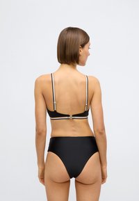 Melns bikini komplekts ar bandejas tipa augšdaļu, kurai ir plānas, regulējamas lences un zelta detaļas, kopā ar augsta vidukļa apakšdaļām. Gluda tekstūra.