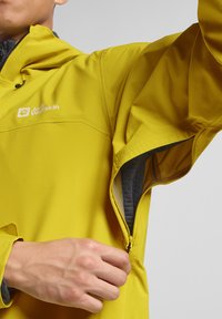 Giacca impermeabile gialla con tasca laterale con zip, dotata di un logo sul petto e realizzata in un tessuto leggero e morbido.