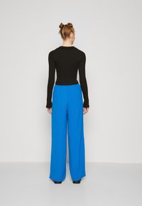 Langermet svart topp med en tettsittende design, kombinert med vide, lyseblå bukser med elastisk midje og glatt tekstur.