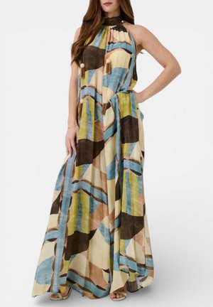 Donna che indossa un vestito senza maniche, a collo alto, lungo fino a terra, con un motivo astratto multicolore in tonalità di blu, verde, marrone e beige.