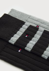 Pair of knitted accessories, one black and one grey, featuring striped patterns and small logo accents in red, white, and blue.