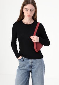 Svart langermet topp kombinert med lyseblå denimjeans. En rød veske bæres over skulderen, som fremhever sin buede form og stropp.