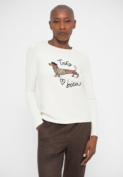 Lange mouwen crèmekleurig shirt met een teckelafbeelding in een gestreepte outfit, met de tekst "Très bien" in een speels lettertype. Zachte stof.