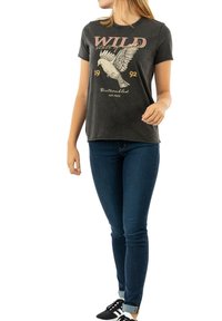 Camiseta de algodón gris oscuro con un gran gráfico de estilo vintage de un pájaro y el texto "WILD 1992" con una textura suave. Combinada con jeans azules.