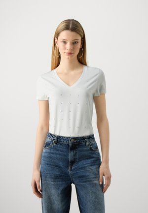 Ανοιχτό μπλε μπλούζα V με κοντά μανίκια, με διακοσμητικό σχέδιο από μικρές σκοτεινές λεπτομέρειες, συνδυασμένη με ψηλόμεσα τζιν παντελόνια.