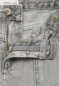 Sive jeans iz džinsa z zadrgo, z kovinsko gumbno zapiralo, razfrkanimi robovi in teksturiranim vzorcem. Oznaka za nego vidna blizu pasu.
