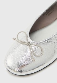 Ασημί μπαλαρίνα με υφή, στρογγυλεμένη μύτη και μικρό διακοσμητικό φιόγκο επάνω.