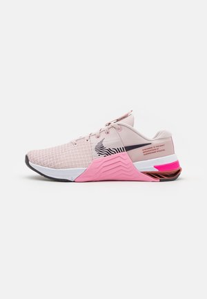 Lichtroze sportschoen met mesh bovenwerk, roze en witte gestructureerde zool, zwarte gebogen streep en roze tekst op het hielgedeelte.