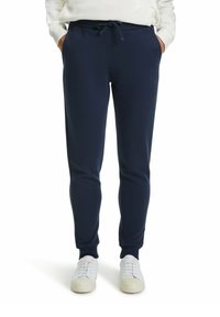 Marineblauwe sweatpants van zachte stof, met een trekkoord in de taille, taps toelopende beenen en zijzakken. Gecombineerd met witte sneakers.