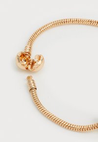 Gullfarget armbånd med et fleksibelt, slange-lignende kededesign. Har en rund lås med en polert finish og vridde detaljer.