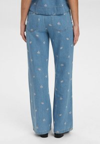 Lichtblauwe denim flared jeans met een bloemenprint, voorzien van twee achterzakken en een licht vervaagde textuur.