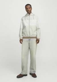 Letvægts hættejakke i lysegrå med hvide paneler, elastiske cuffe og snoretræk. Kombineret med løse, faldne denim og brune støvler.