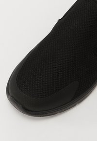 Zwarte sportieve schoen met een ademende mesh bovenkant en een gladde rubberen zool. Gestructureerd oppervlak zonder zichtbare logo's of patronen.