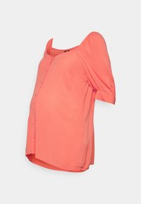 Blusa premaman corallo con bottoni, maniche a sbuffo, tessuto morbido e orlo curvo, progettata per offrire comfort durante la gravidanza.