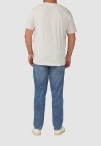 Hellbeige Baumwoll-T-Shirt mit kurzen Ärmeln, kombiniert mit mittelblauen Jeans. Weiße Sneakers mit hellen Sohlen.