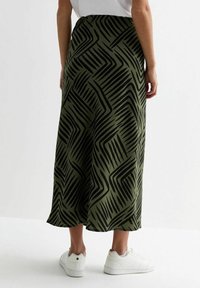 Jupe maxi vert olive avec un motif zigzag noir, en tissu lisse, dotée d'un design fluide et d'un ourlet légèrement évasé.