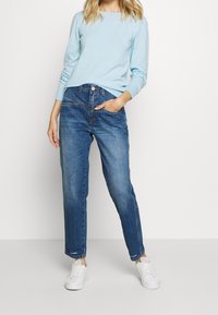 Pull bleu clair à manches longues avec poignets côtelés, associé à un jean droit d'ampleur moyenne. Des baskets blanches complètent la tenue.