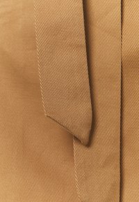 Ljusbrun tyg med en subtil ribbad textur; har vikta kanter och en smidig yta. Designen är enkel och funktionell.