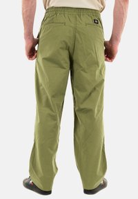Pantalones cargo de algodón ligeros y verdes con cintura elástica, dos bolsillos traseros y un corte holgado, combinados con zapatillas negras.